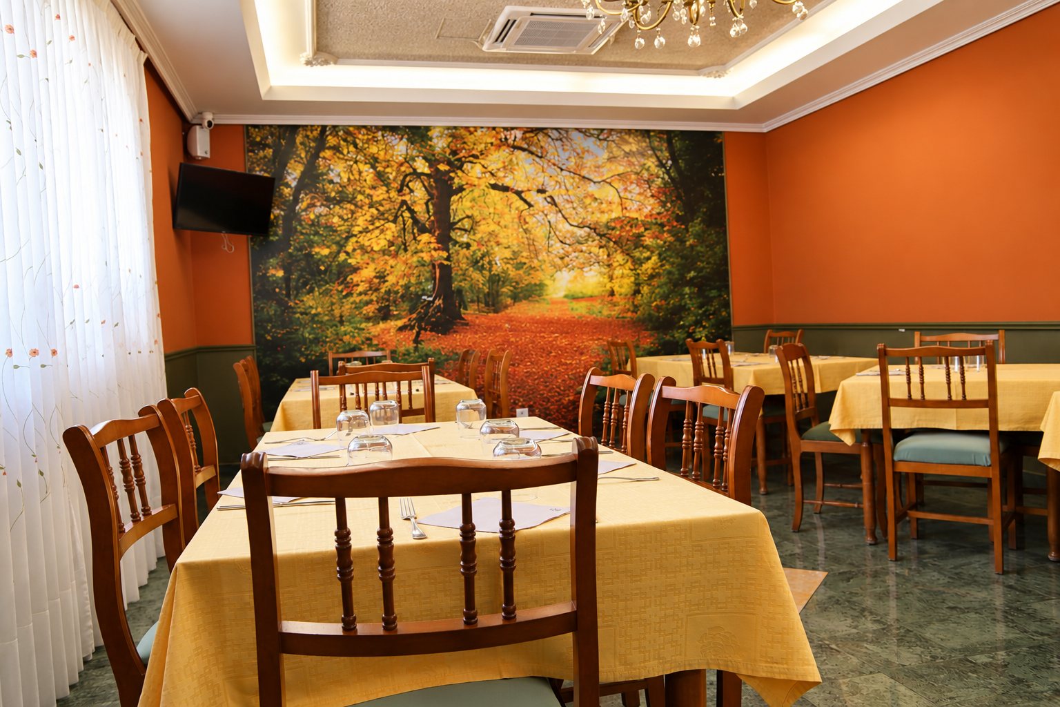 Salón con mesas de mantel amarillo y un gran mural de un bosque en otoño.