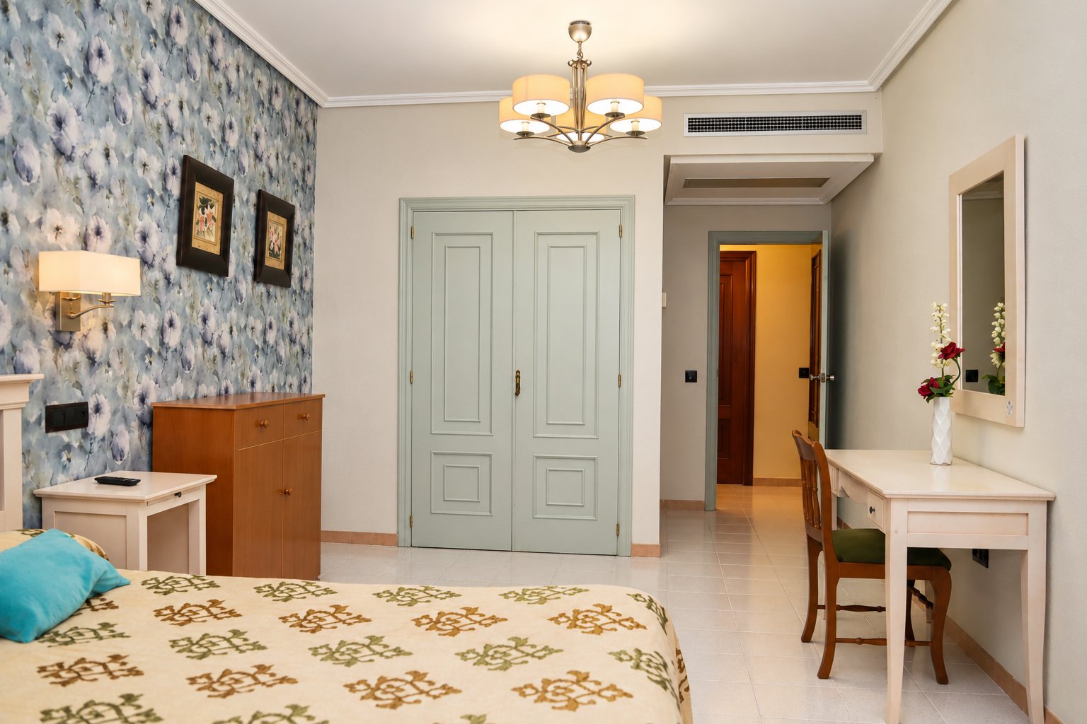 Habitación con cama, escritorio blanco, lámpara de techo y puerta de doble hoja.