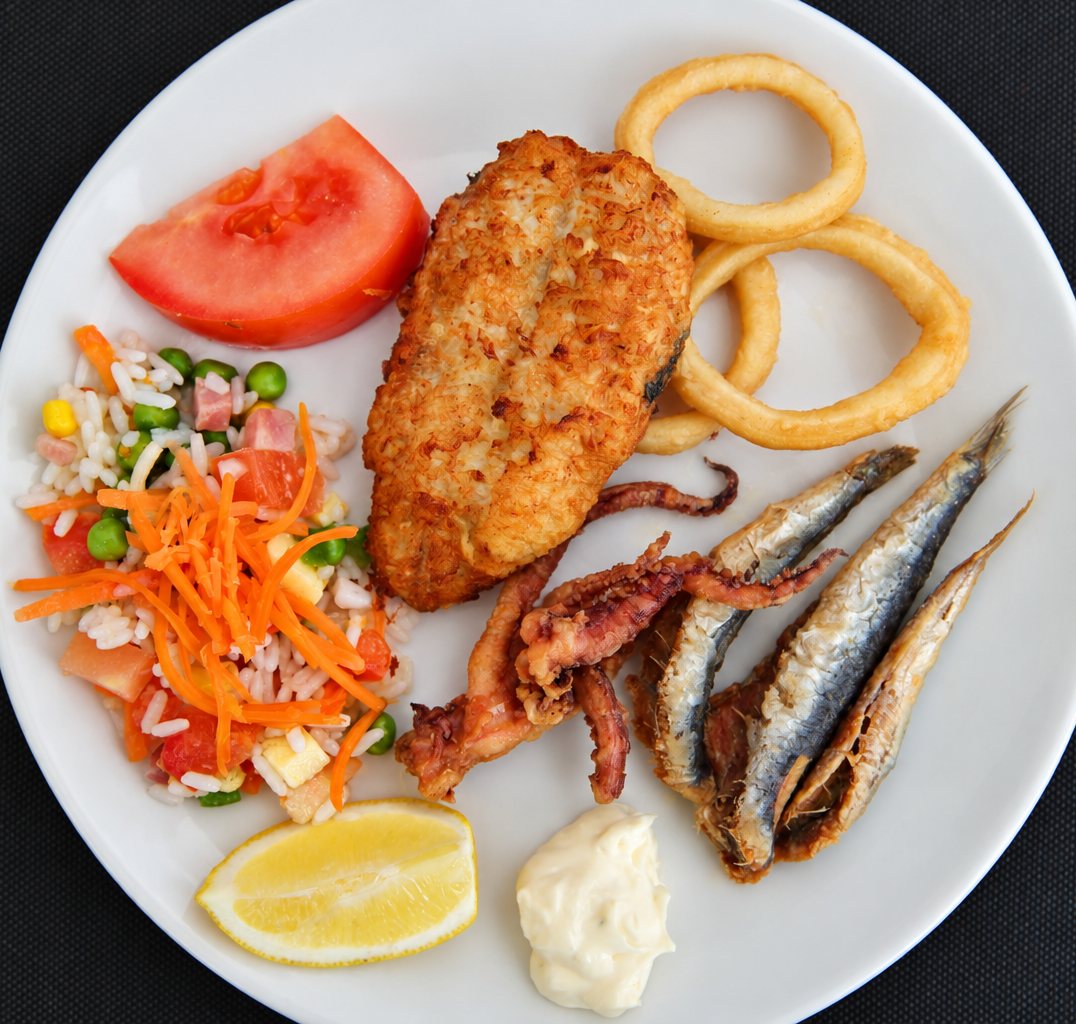 Plato combinado visto desde arriba: pollo empanado, pescado frito, calamares, ensalada, tomate y limón.
